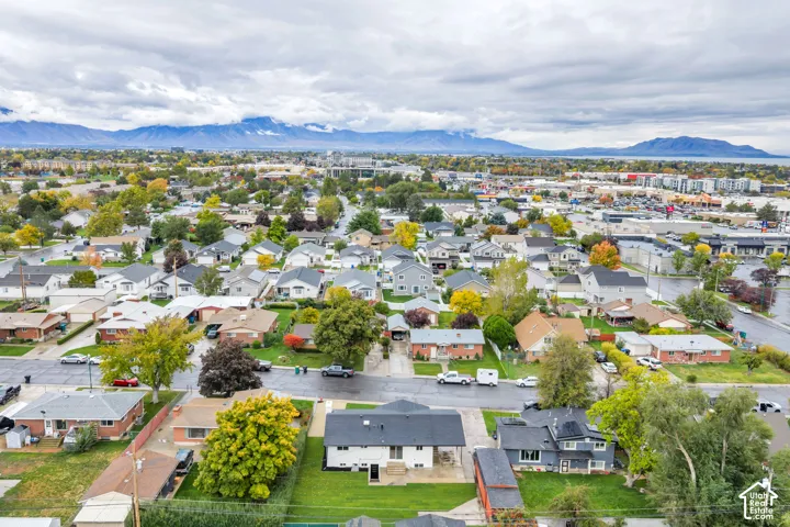 Aerial perspective featuring a detached residential property with a multi-gabled roof, covered patio, mature landscaping, and mountain backdrop