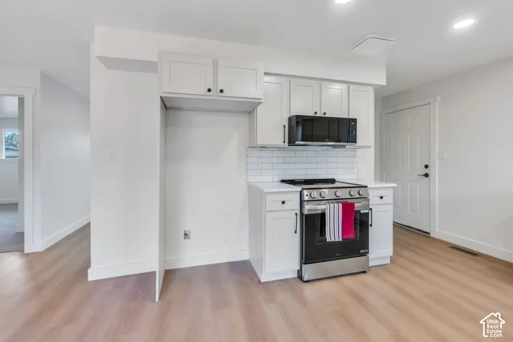 Kitchen featuring white cabinetry, subway tile backsplash, solid-surface countertops, and stainless steel appliances with wood-finish flooring