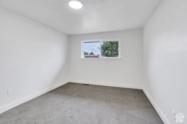 Neutral-toned walls, grey carpeting, and a single sliding window with a frame finish