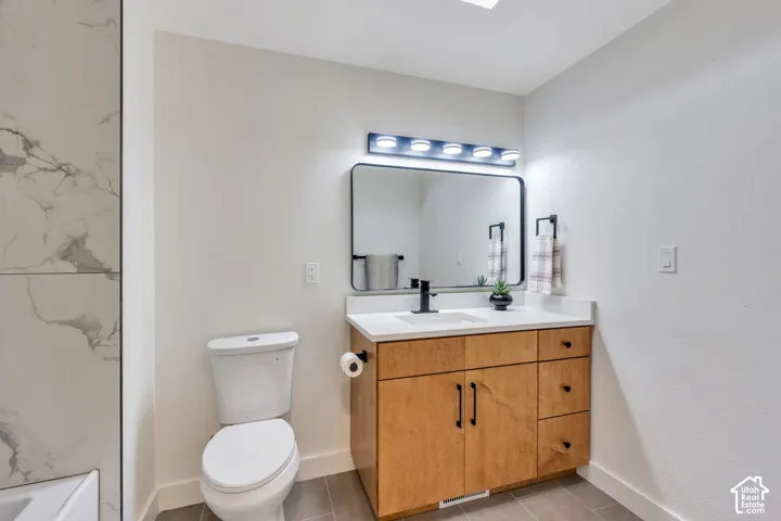 Natural wood-finish vanity with a white countertop, rectangular undermount sink, matte black faucet, and matching cabinet hardware, paired with a framed mirror and tiled shower surround
