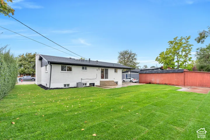 Exterior rear elevation featuring white painted brick masonry, dark shingle roofing, concrete stairs, fenced perimeter, and a grass lawn