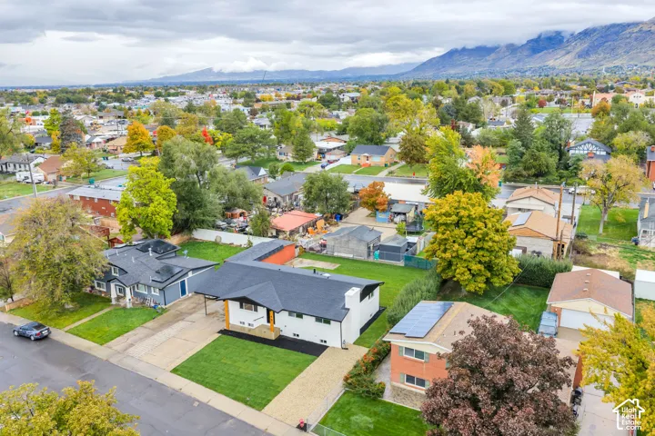 Single-story residence featuring a dark shingled roof, white exterior siding, a front carport, and a manicured lawn, set against a mountainous horizon