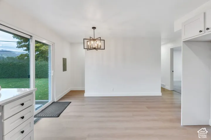 Wood-finish flooring, sliding glass door, geometric chandelier, white cabinetry, and quartz countertops