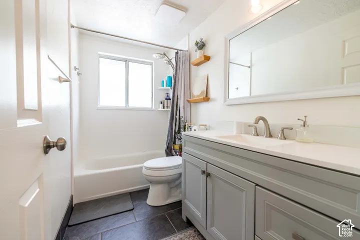 Bathroom featuring a vanity with a white countertop and satin nickel faucet, framed mirror, dark tile flooring, and a tub-shower combination with a surround