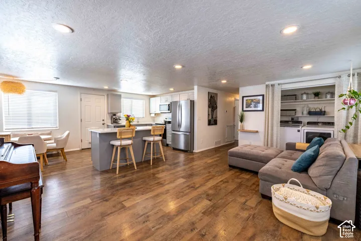 Open-concept kitchen featuring an island with stone-finish countertops, wood-finish flooring, recessed lighting, and a built-in laundry area