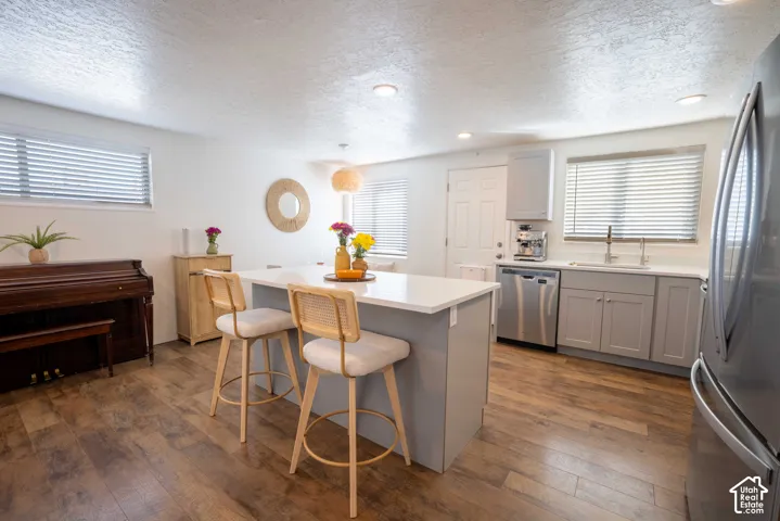 Kitchen featuring a central island with a solid-surface countertop, wood-finish flooring, grey cabinetry, stainless steel appliances, and recessed lighting