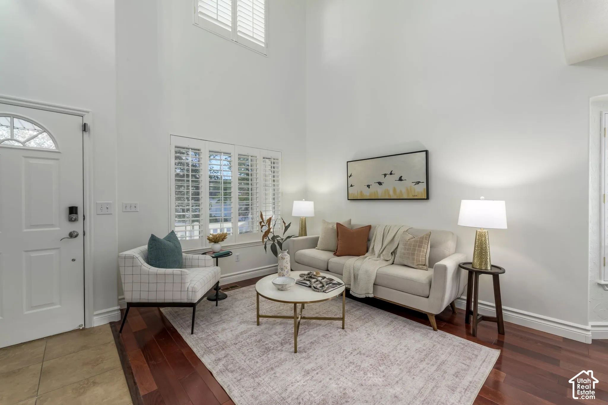 Vaulted ceilings with expansive wall height, wood-finish flooring, plantation shutters, and a multi-panel entrance door