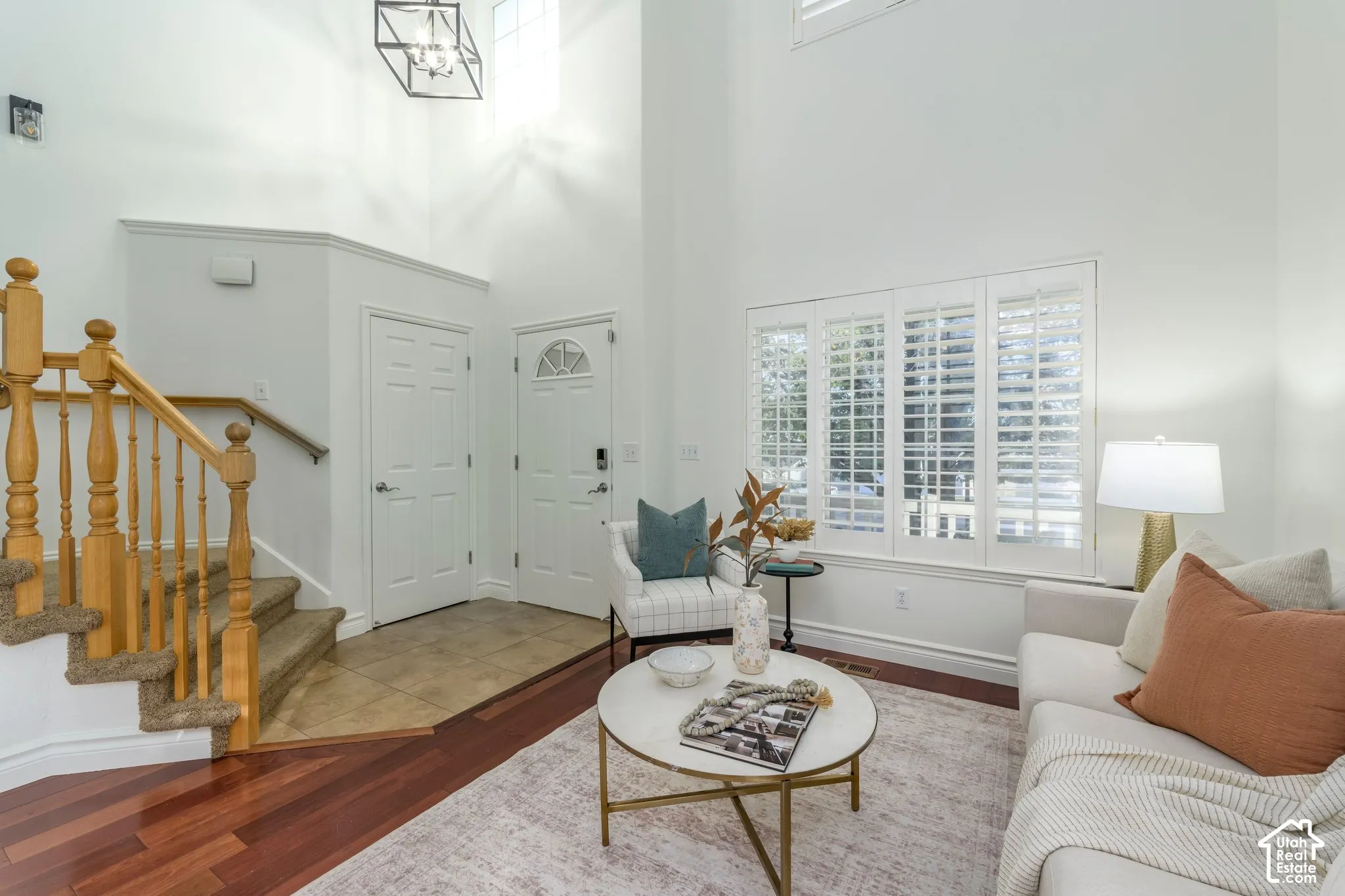 Two-story ceiling height, wood-finish flooring, tile entryway, staircase with wooden balusters, and multi-pane window with plantation shutters