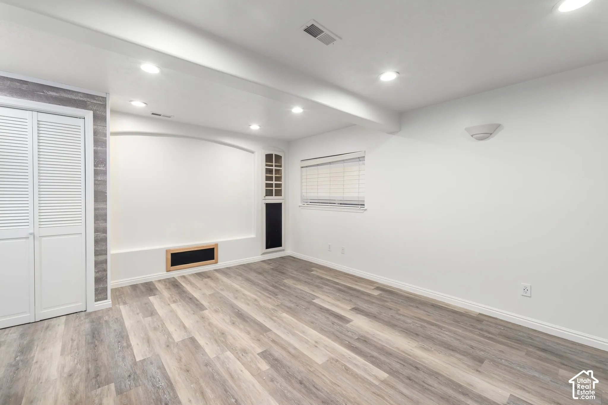 Room featuring wood-finish flooring, recessed lighting, white bifold closet doors, a recessed wall niche with built-in shelving, and a multi-pane window with blinds