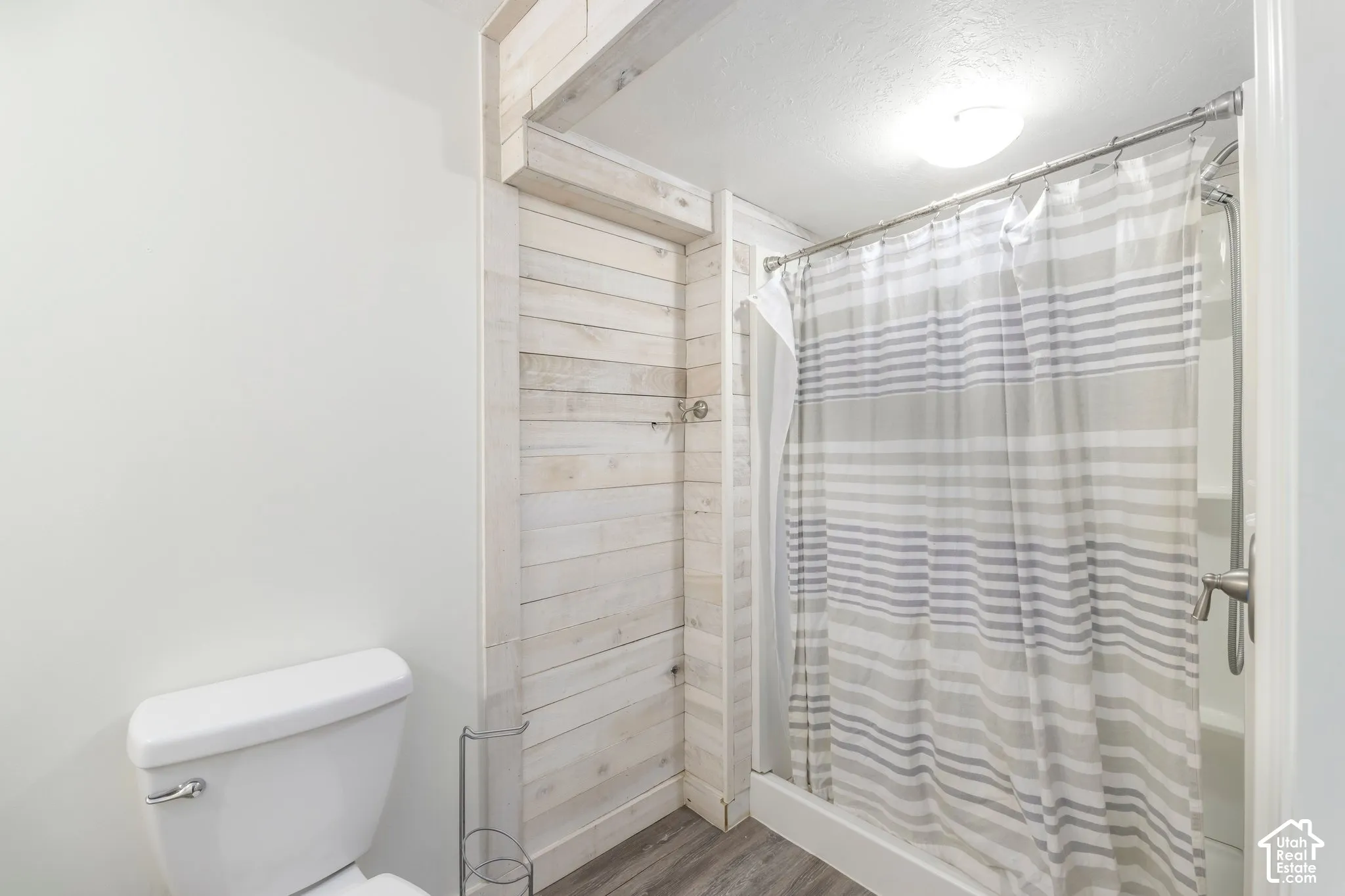 Bathroom featuring light-toned horizontal wood-plank wall accent, wood-finish flooring, and a tub-shower combination with metallic fixtures