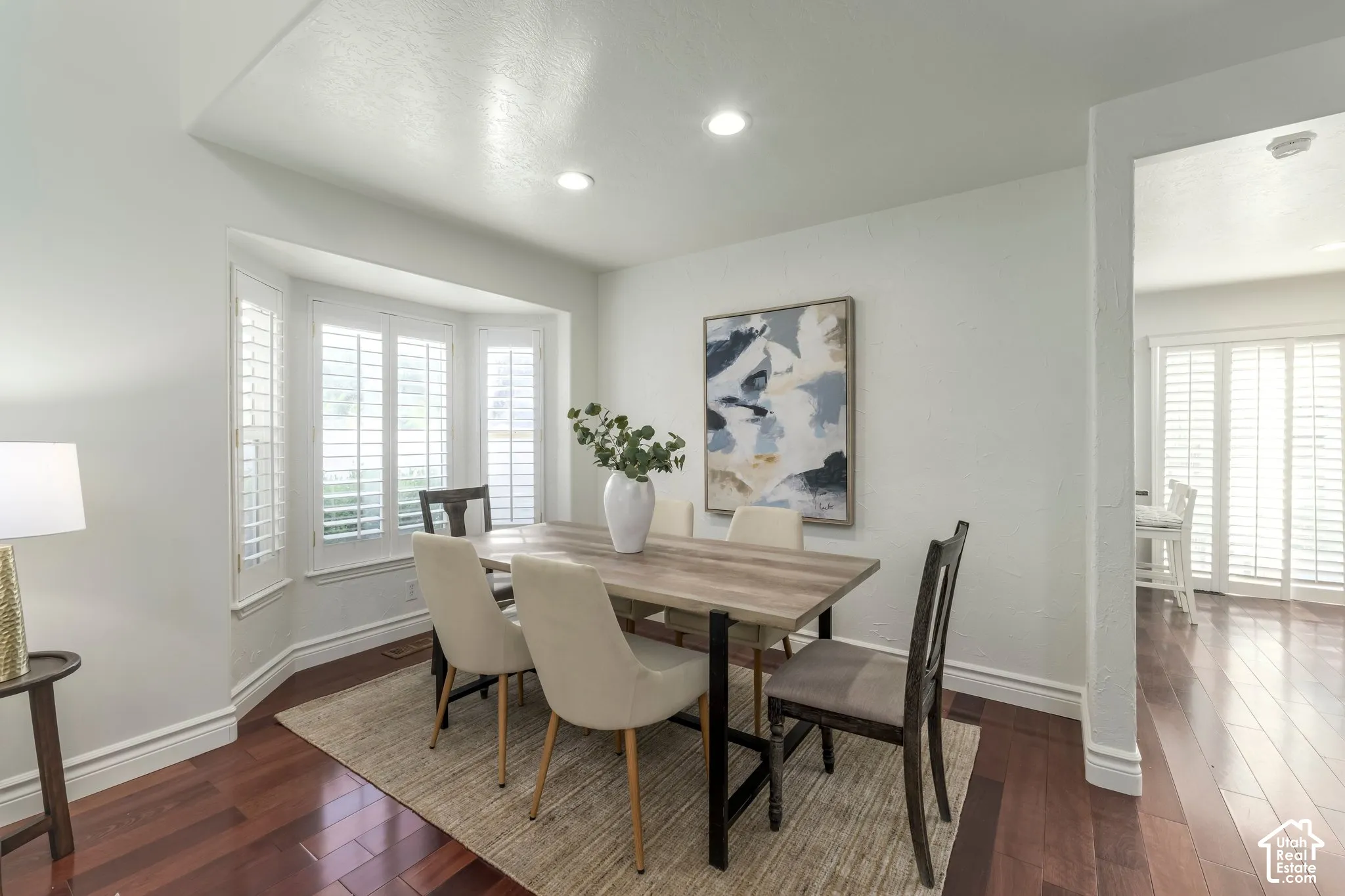 Dining area featuring bay windows with plantation shutters, recessed lighting, and wood-finish flooring