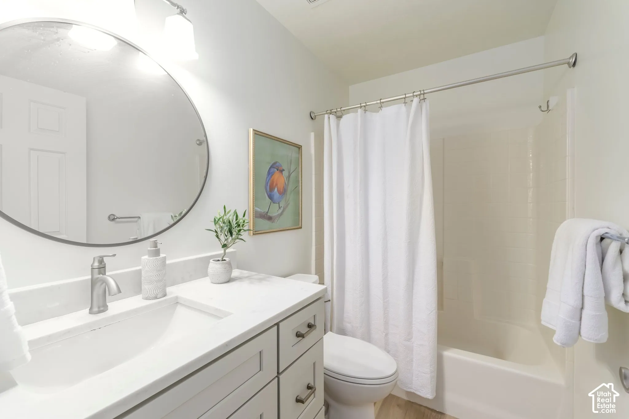 Bathroom featuring a vanity with a light-toned countertop, integrated basin, and brushed nickel hardware, paired with a circular mirror, wall-mounted lighting, and a shower-tub combination with a tiled surround