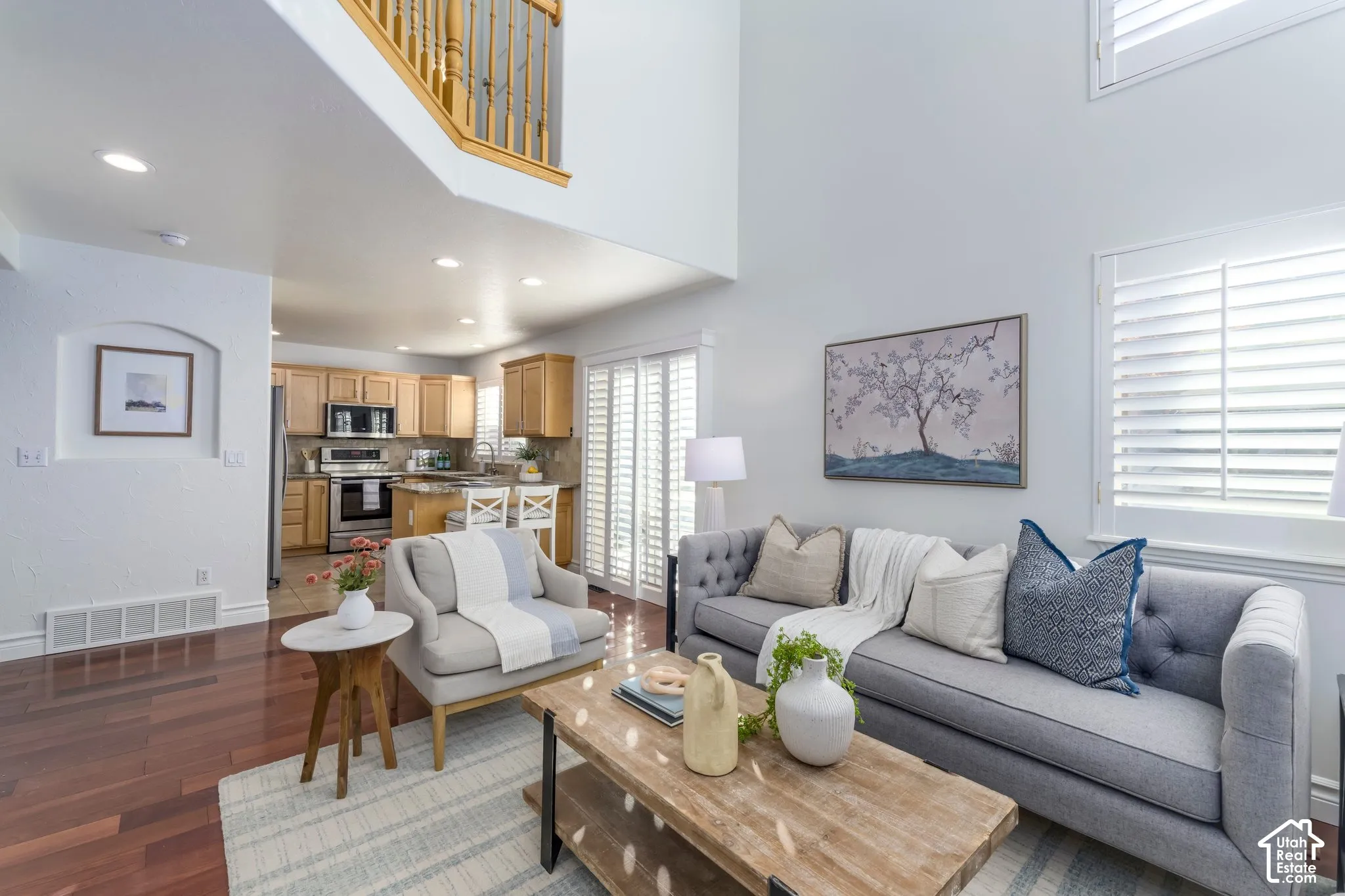 High-ceilinged living area featuring wood-finish flooring, recessed lighting, white plantation shutters, and a recessed wall niche
