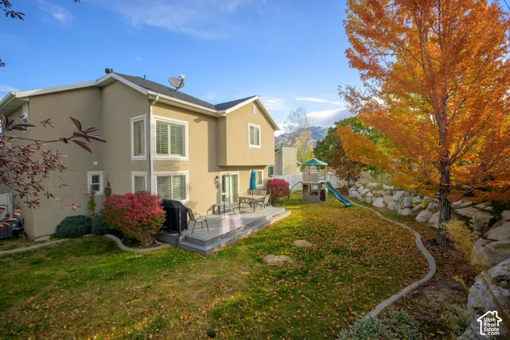 Two-story stucco exterior, raised deck, terraced rock retaining wall, and mature trees on the property