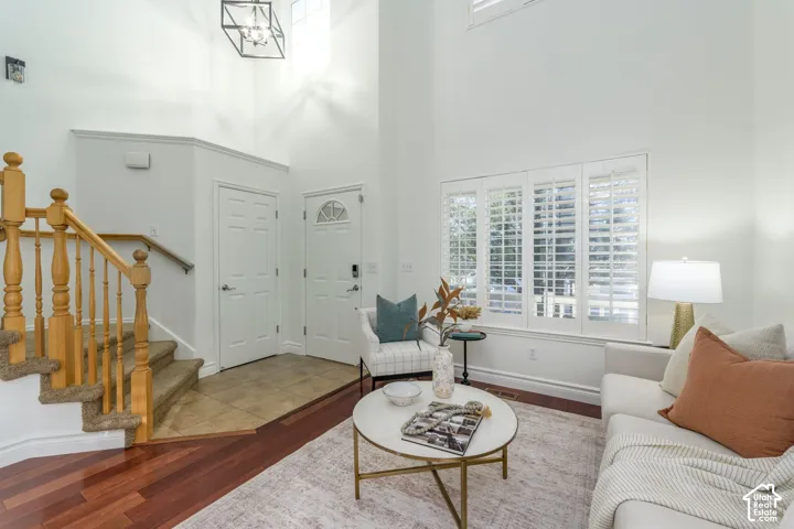Two-story ceiling height, wood-finish flooring, tile entryway, staircase with wooden balusters, and multi-pane window with plantation shutters