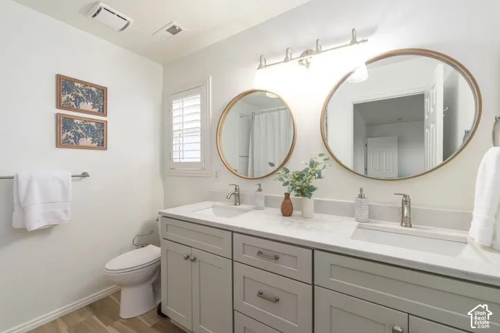 Dual-sink vanity with neutral-toned cabinetry, light-colored stone-finish countertop, round gold-tone framed mirrors, and wood-finish flooring