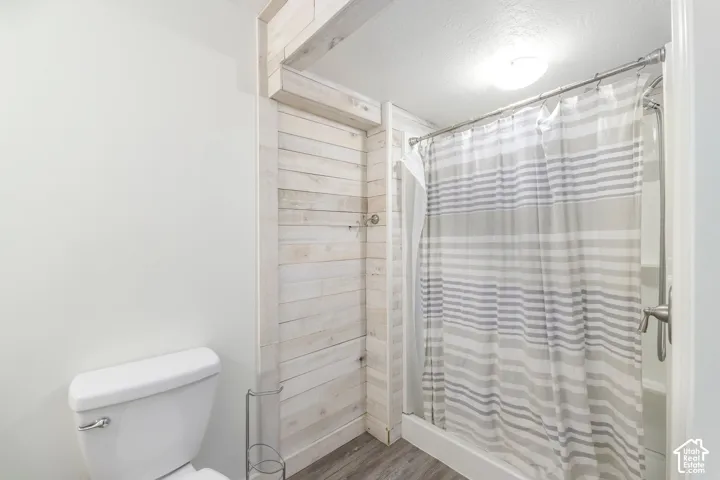 Bathroom featuring light-toned horizontal wood-plank wall accent, wood-finish flooring, and a tub-shower combination with metallic fixtures