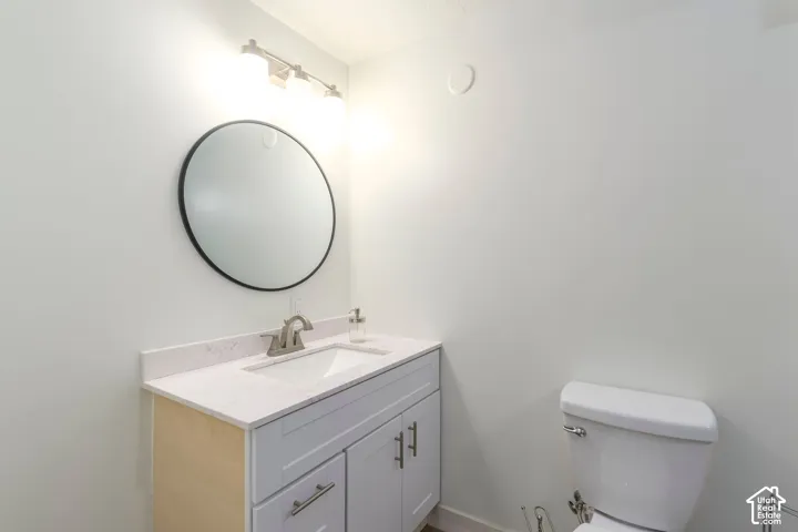 White vanity with a neutral stone-look countertop, integrated rectangular sink, round wall-mounted mirror, and three-light fixture