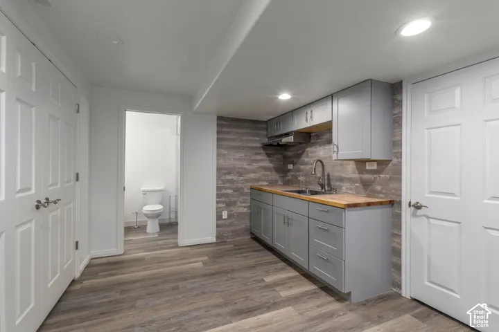 Kitchenette featuring grey shaker-style cabinetry, wood-finish countertop, plank-style backsplash, and wood-finish flooring, with a dedicated water closet