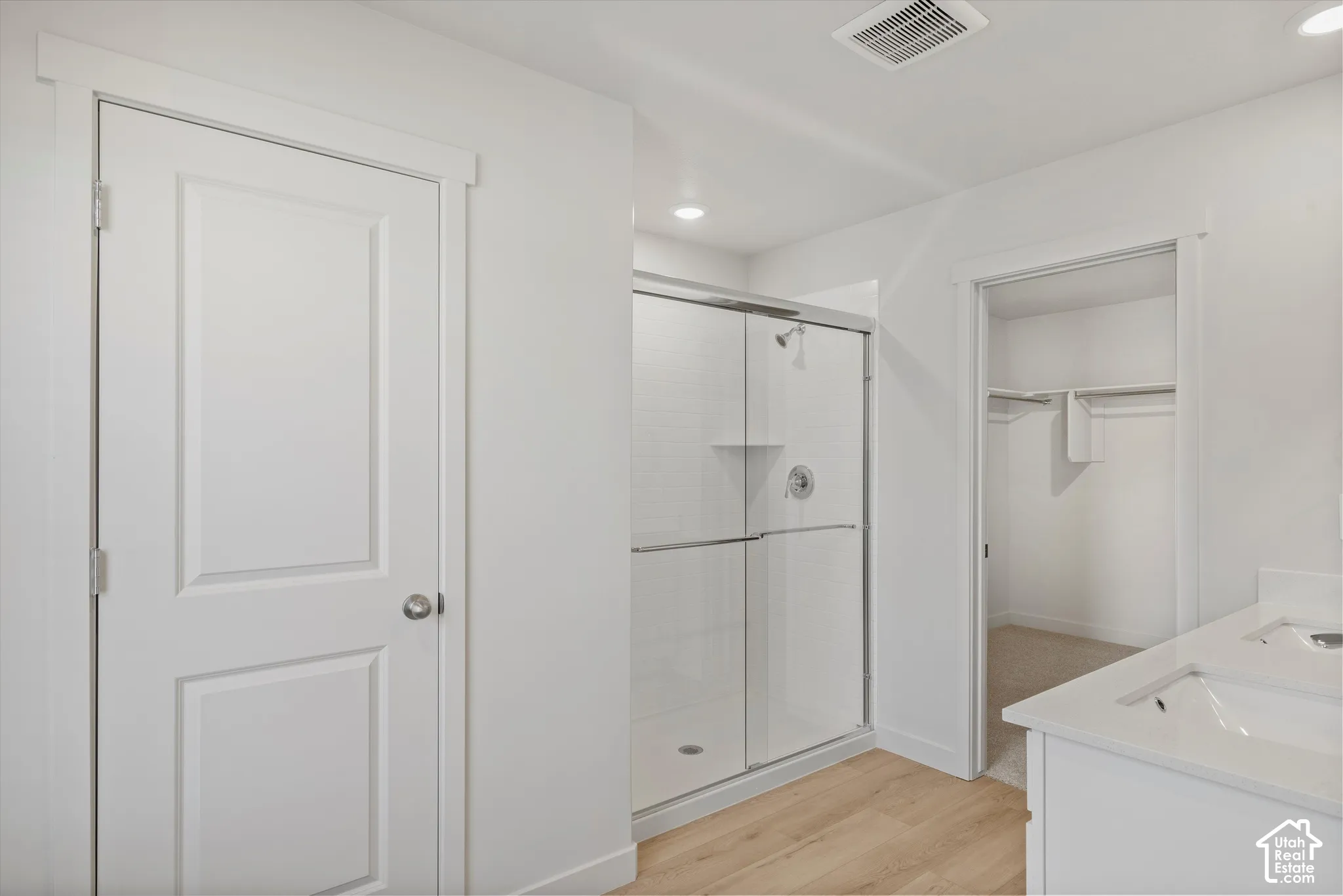 Walk-in shower with a glass enclosure, dual-sink vanity with a solid-surface countertop, and a built-in closet with shelving