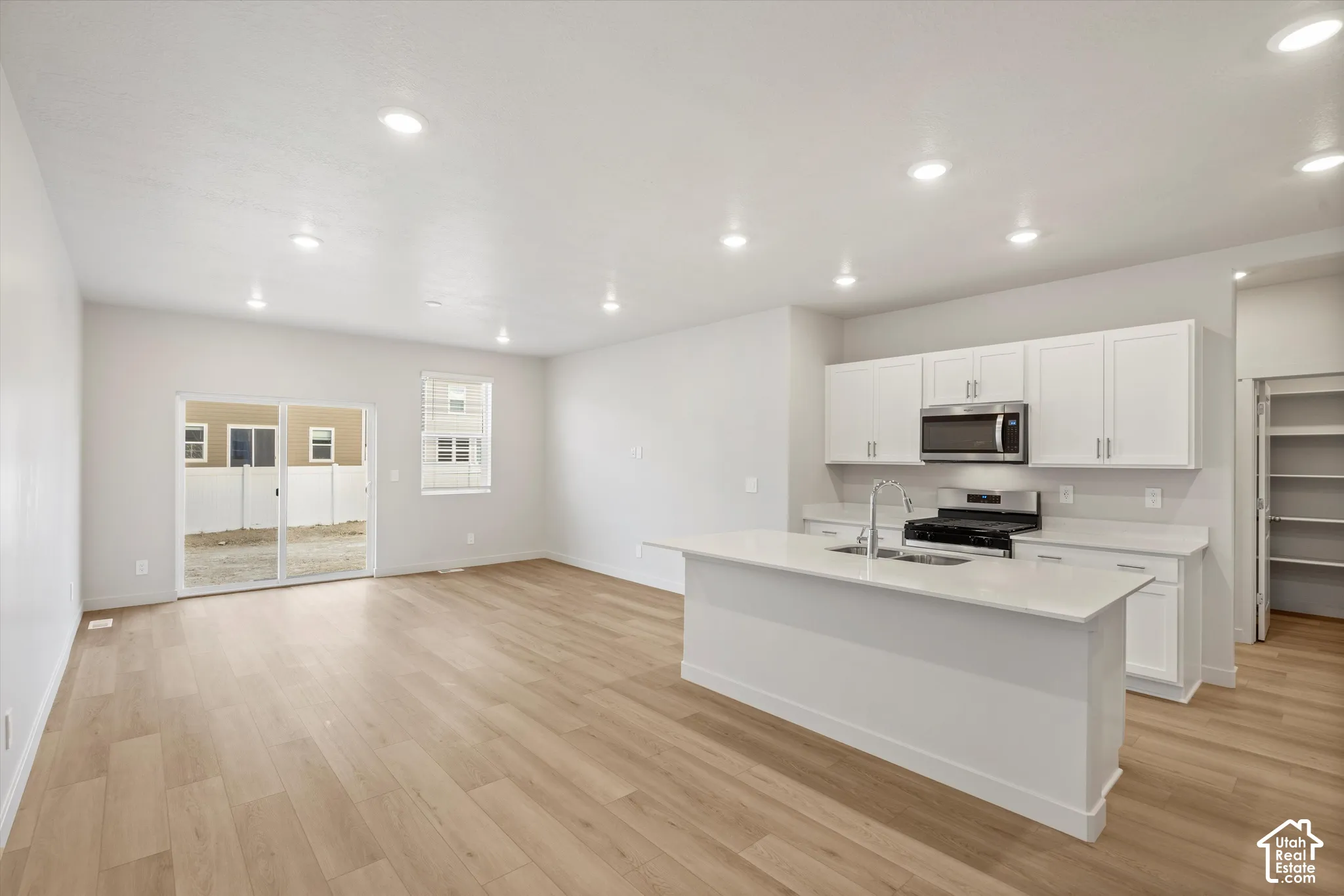 Open-concept interior featuring light wood-finish flooring, a kitchen island with stone-finish countertops, crisp white cabinetry, recessed lighting, and a sliding glass door