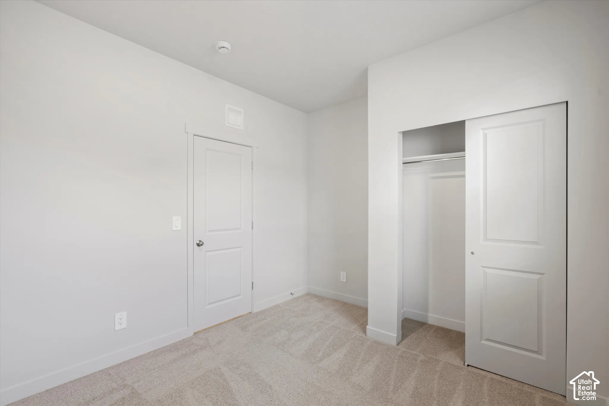 Neutral interior space featuring high ceilings, light-toned wall-to-wall carpeting, a sliding panel closet door, and a solid-core two-panel interior door