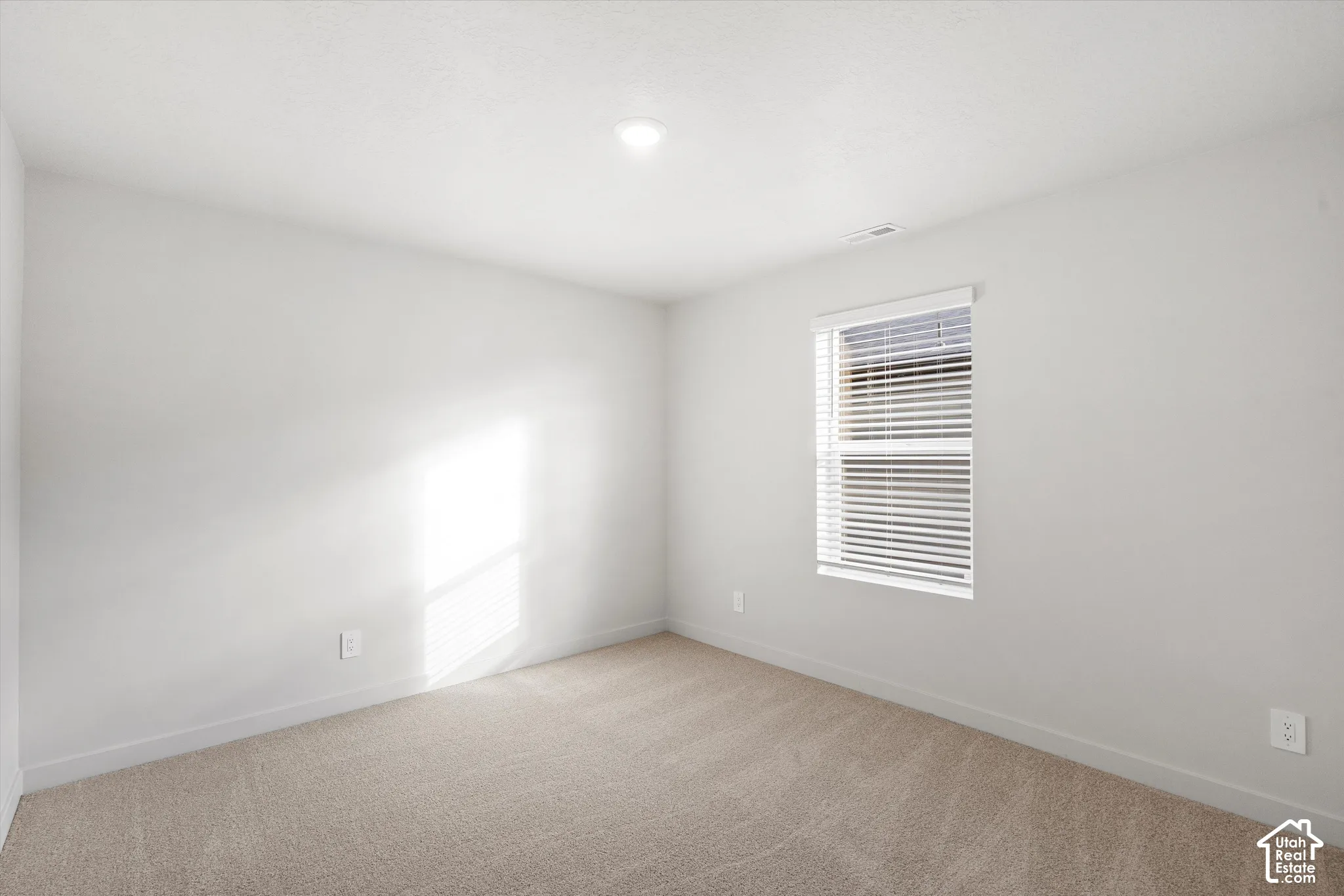 Neutral-toned carpeted flooring, white wall finishes, and a window equipped with horizontal blinds and a recessed lighting fixture