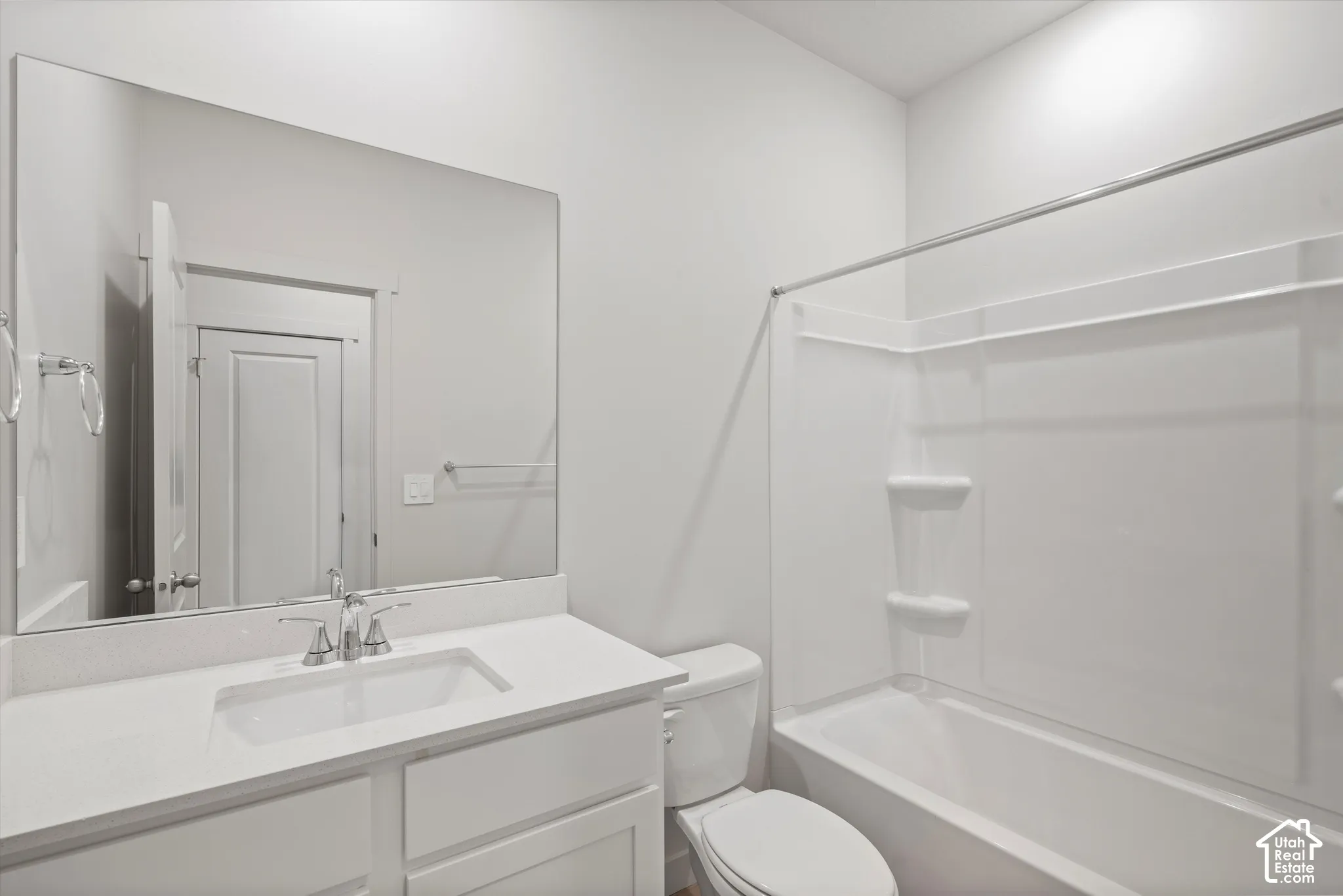 Bathroom featuring a white vanity with a rectangular sink, expansive frameless mirror, chrome faucet, and integrated tub and shower combination with recessed shelving