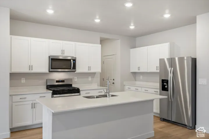 Kitchen featuring white cabinetry, solid-surface countertops, center island with integrated sink, stainless steel appliances, and recessed lighting