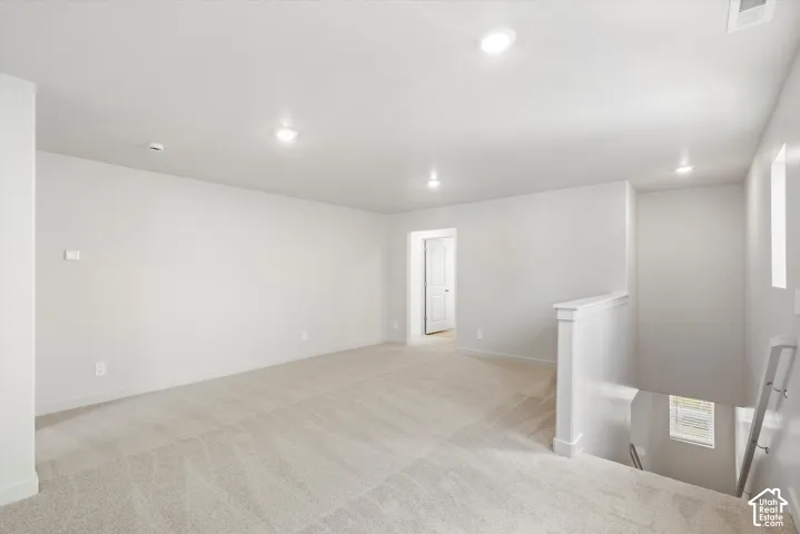 Neutral-toned wall-to-wall carpeting, recessed ceiling lighting, and a painted wood banister with a handrail
