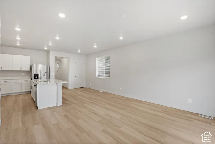 Interior space featuring wood-finish flooring, recessed lighting, white cabinetry, a kitchen island with stone-surface countertop, and stainless steel appliances