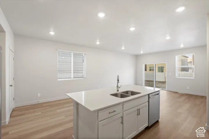 Kitchen featuring a central island with a solid-surface countertop, stainless steel dual-basin undermount sink, built-in dishwasher, and wood-finish flooring illuminated by recessed lighting