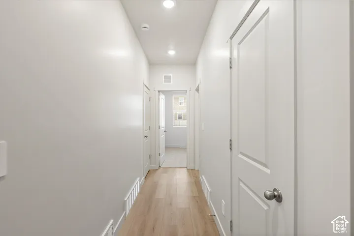 Hallway featuring wood-finish flooring, recessed lighting, and white interior doors with satin nickel hardware