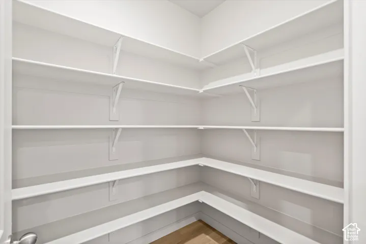 Storage area featuring multi-level wrap-around shelving with white support brackets and wood-finish flooring