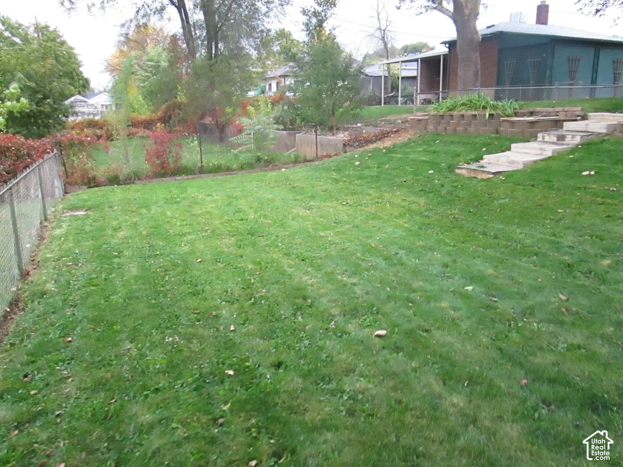 Expansive backyard featuring a tiered lawn, stone retaining walls, concrete steps, and mature trees