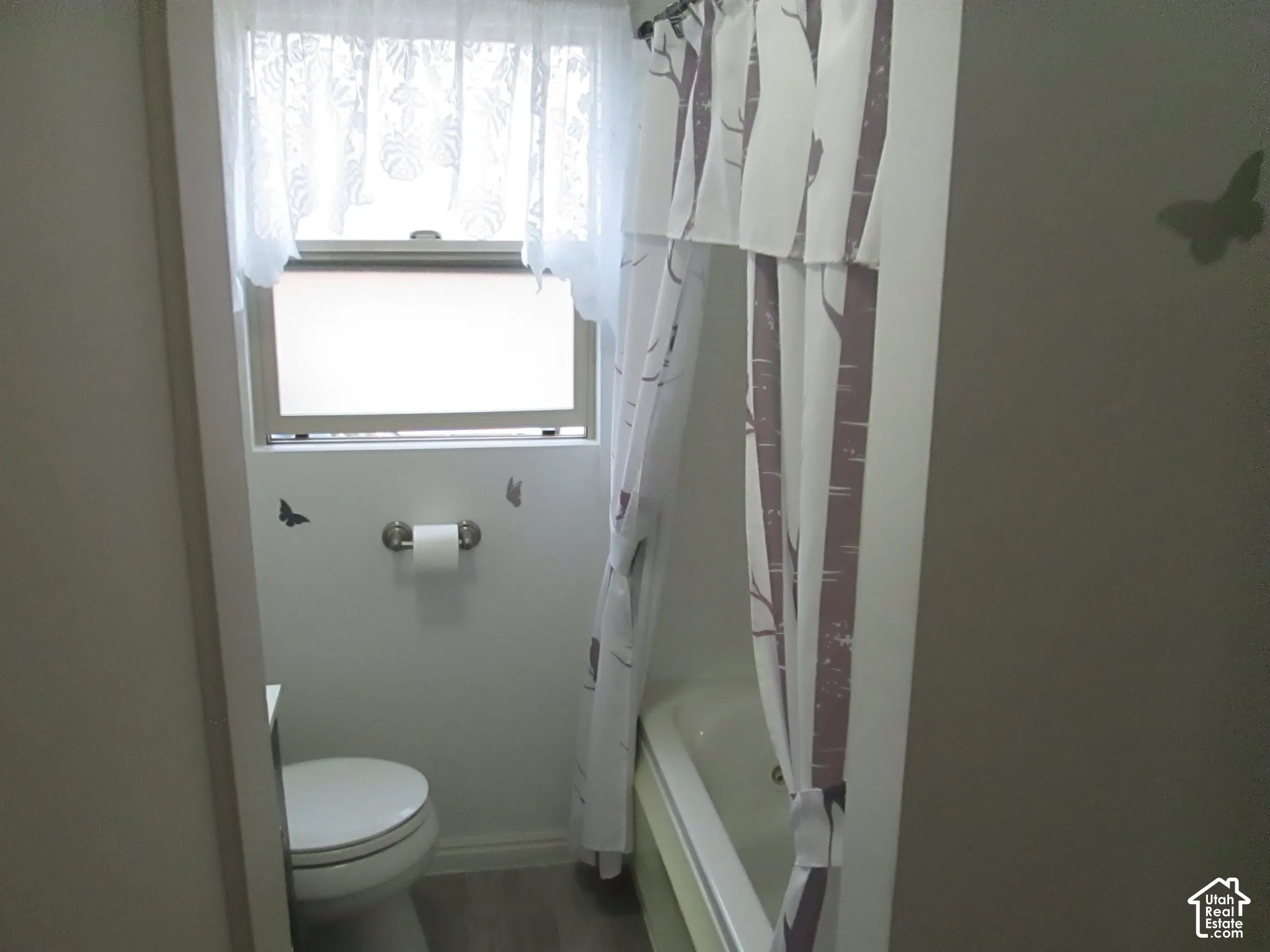 Bathroom featuring a soaking tub, window with natural light, wall-mounted toilet paper holder, and wood-finish flooring