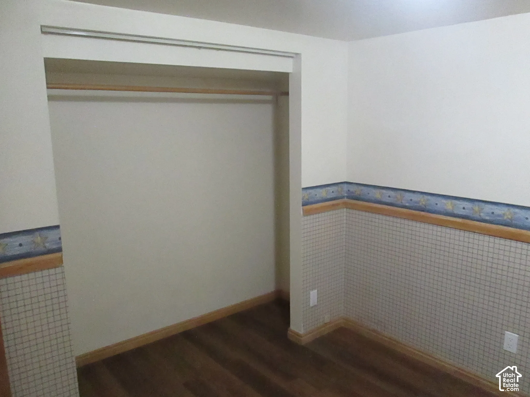 Built-in closet with overhead rod, wood-finish flooring, and decorative chair rail molding with wallpapered wainscoting