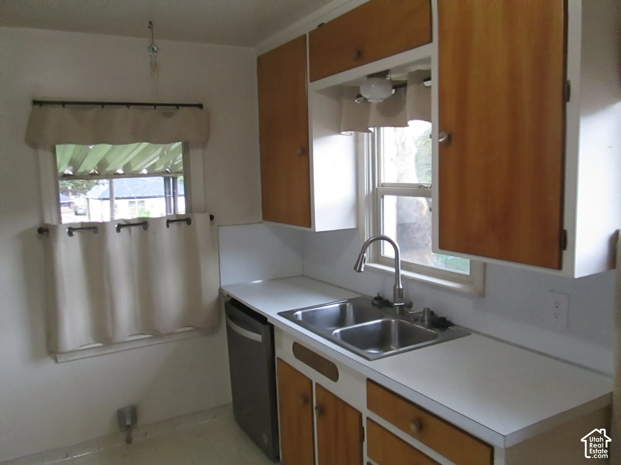 Kitchen featuring wood-finish cabinetry, stainless steel double-basin sink, high-arc faucet, and solid-surface countertops