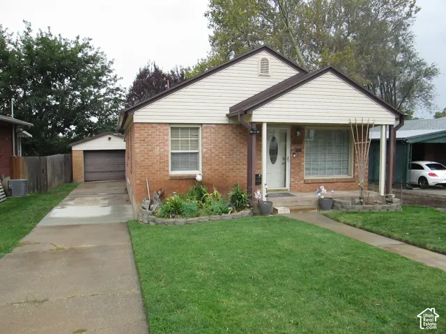 Single-story exterior featuring brick and siding construction, covered front porch, concrete driveway, detached garage, and tiered stone garden beds