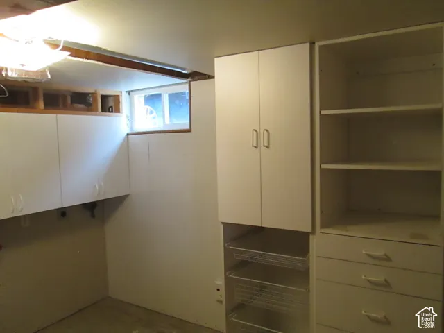 Built-in white cabinetry featuring upper storage units, open shelving, pull-out wire drawers, and integrated flat-panel drawers, complemented by a rectangular slider window