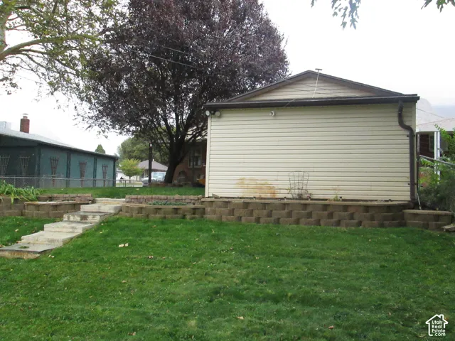 Backyard featuring a tiered stone retaining wall, concrete steps, and expansive lawn space