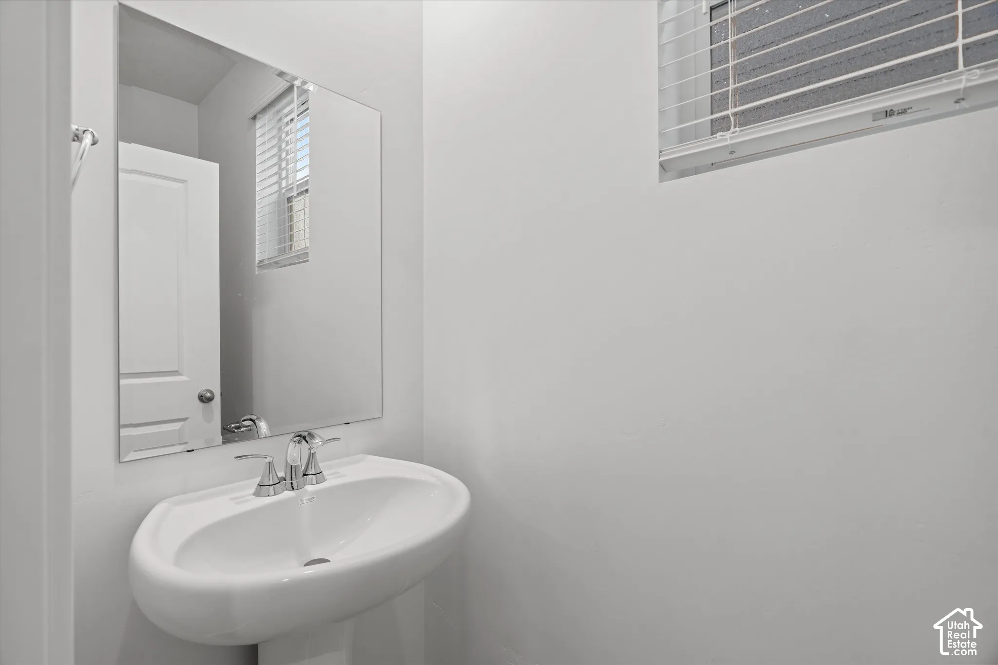 Wall-mounted pedestal sink featuring a chrome dual-handle faucet and a frameless mirror