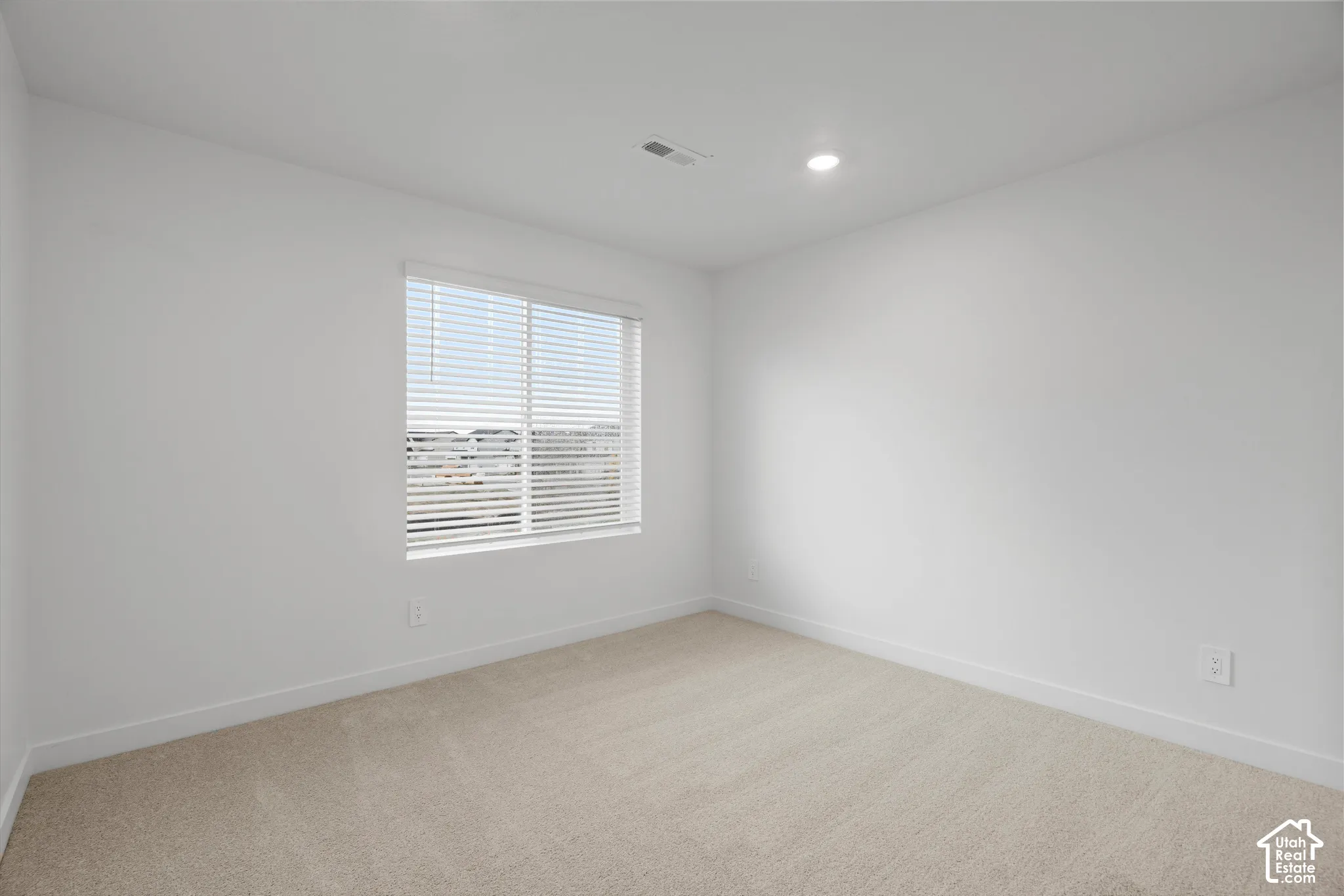 Neutral-toned interior space featuring wall-to-wall carpeting, recessed ceiling lighting, and a single-pane window with horizontal blinds