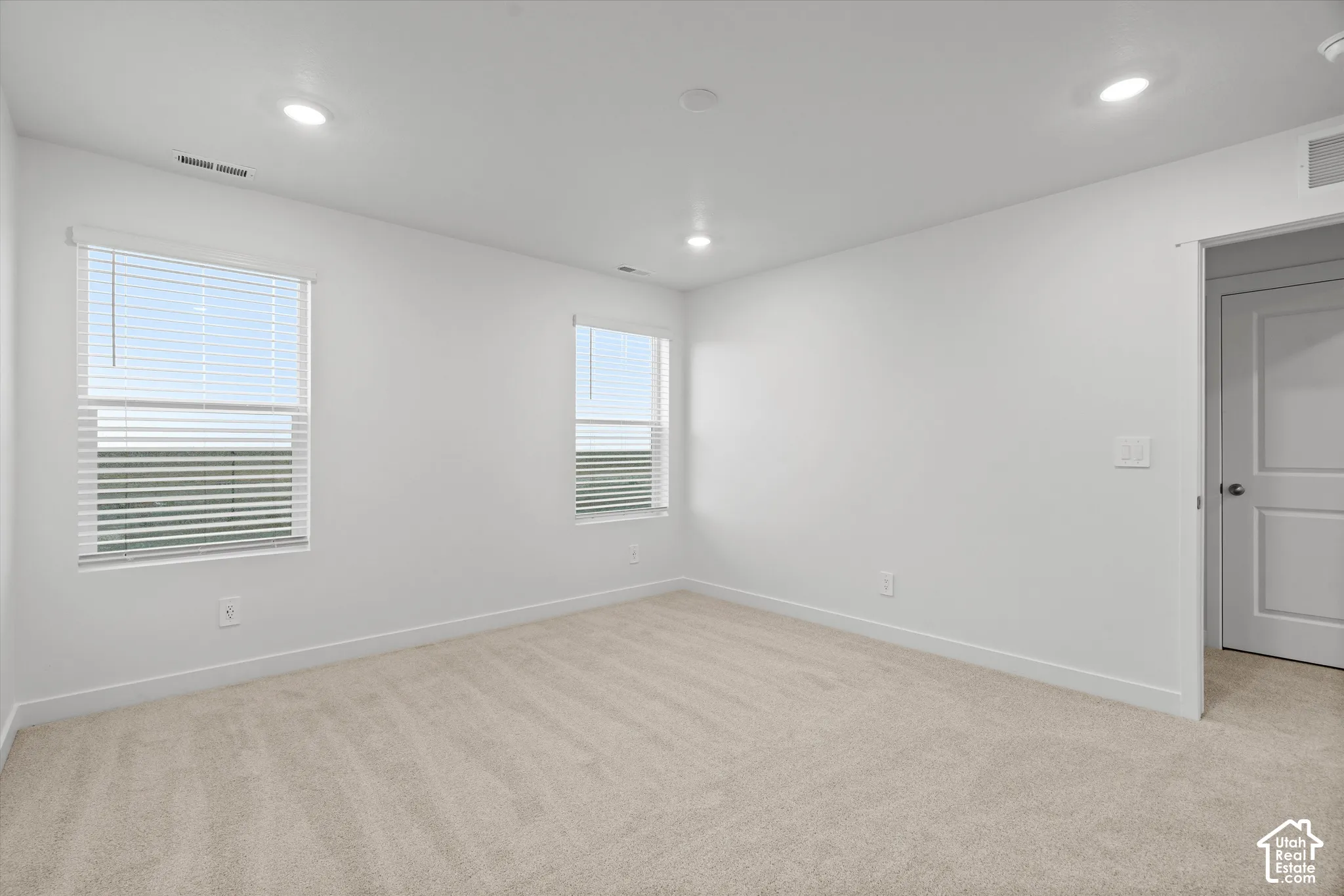 Neutral-toned wall-to-wall carpeting, recessed LED lighting, dual windows with fitted blinds, and a solid-core interior door