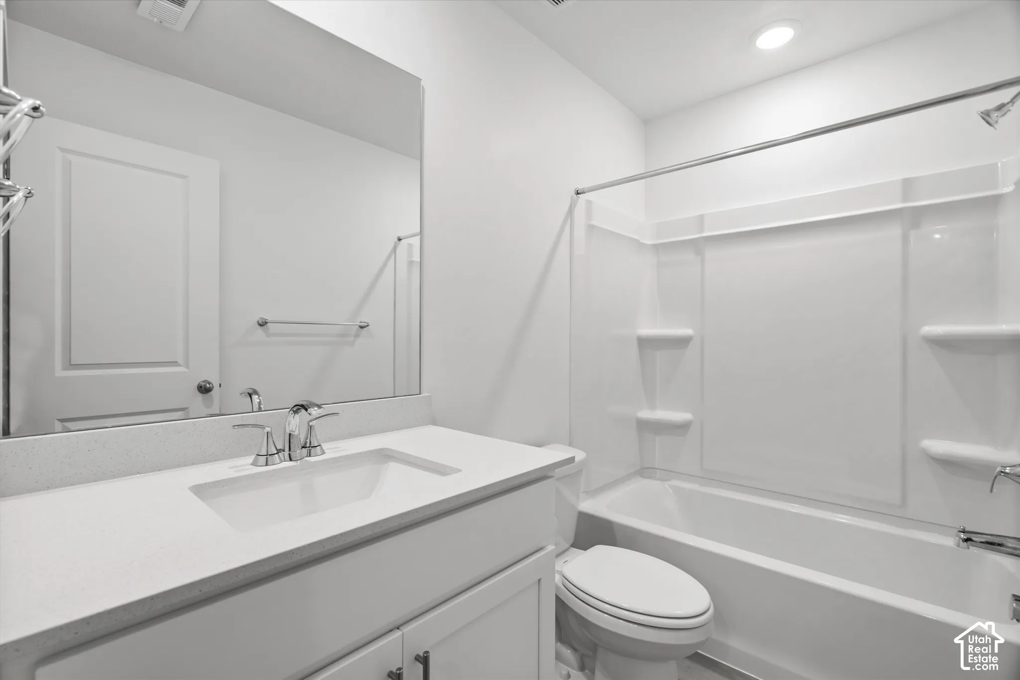 Bathroom featuring a white vanity with a solid-surface countertop, rectangular undermount sink, expansive wall-mounted mirror, and a tub-shower combination with integrated shelving
