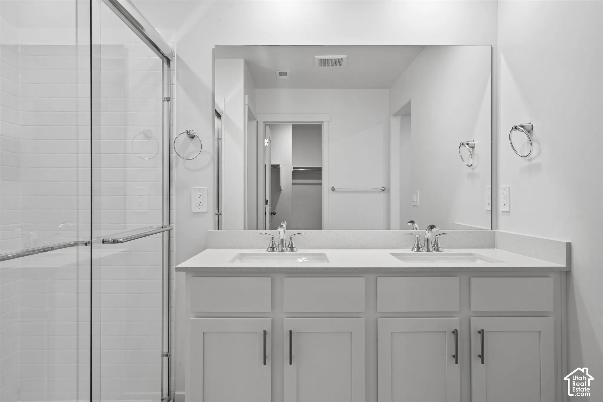 Dual-sink vanity with white shaker-style cabinetry, stone-composite countertop, full-width mirror, and a glass-enclosed shower with tiled surround