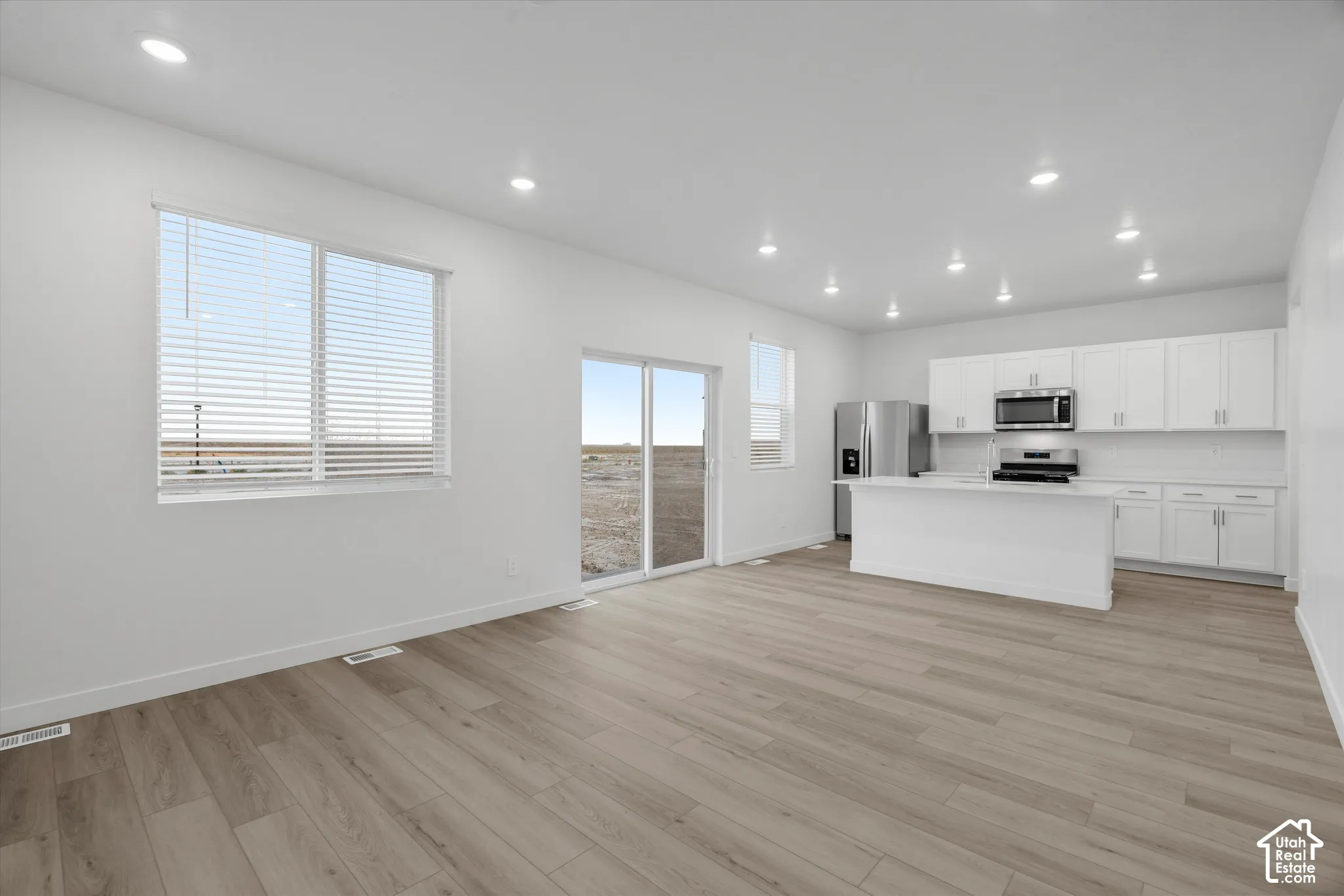 Open-concept interior featuring wood-finish flooring, recessed lighting, white cabinetry, a center island, and glass sliding doors