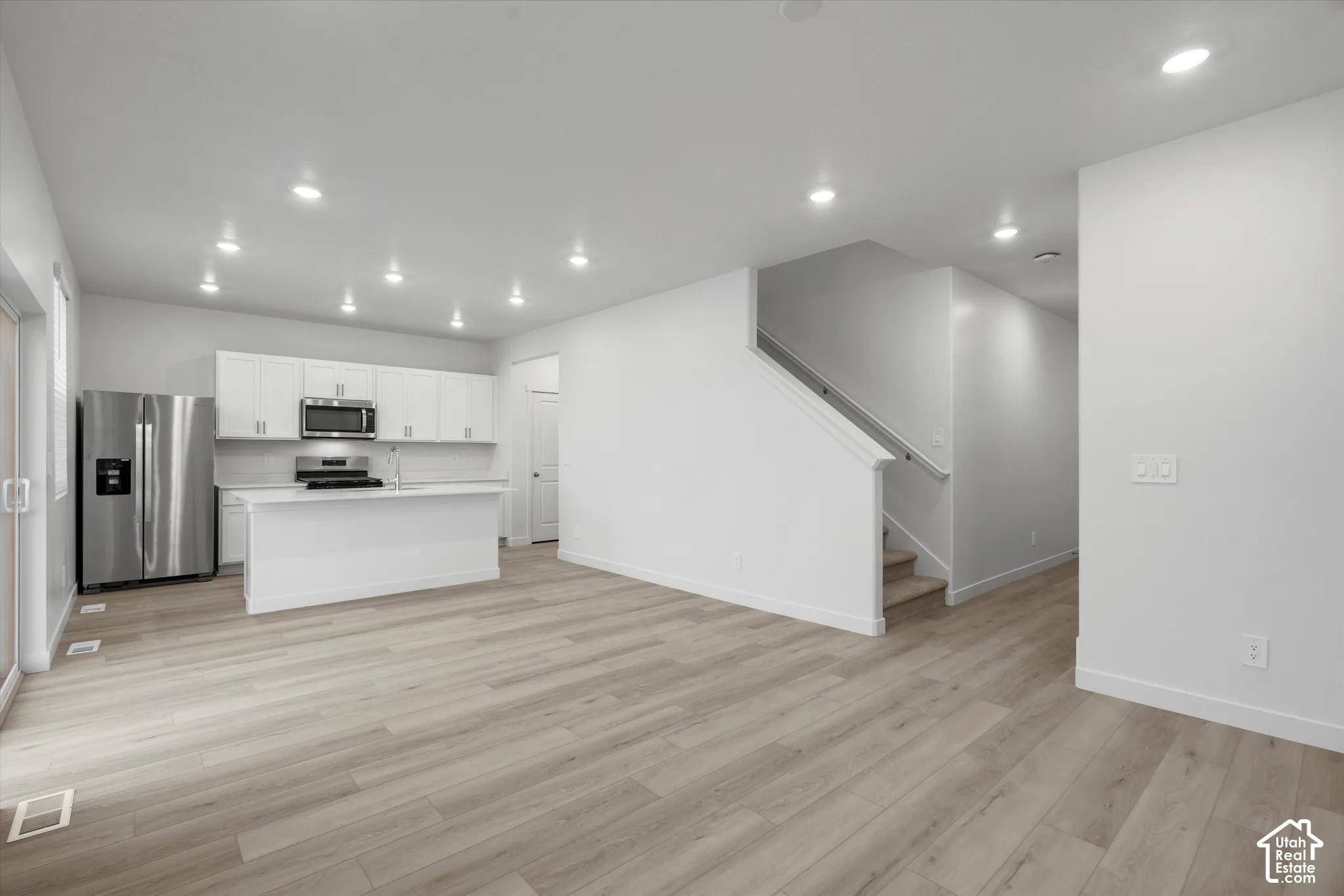 Kitchen featuring white cabinetry, an island, and stainless steel appliances, complemented by wood-finish flooring and recessed lighting