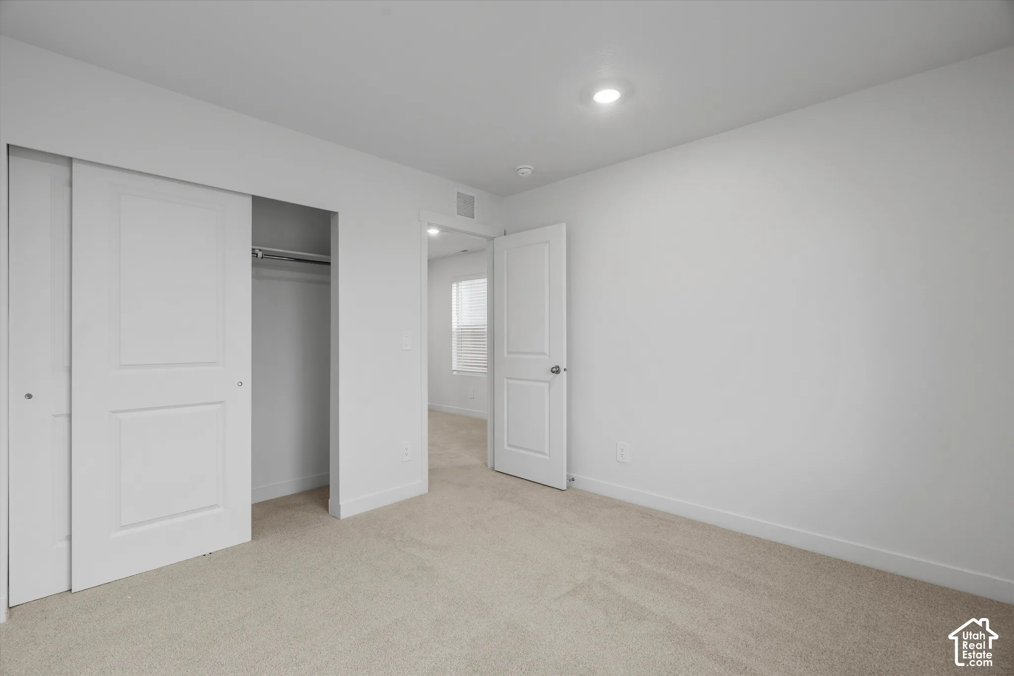 Neutral-toned carpeting, recessed ceiling lighting, sliding closet doors with two-panel detailing, and a solid-core interior door