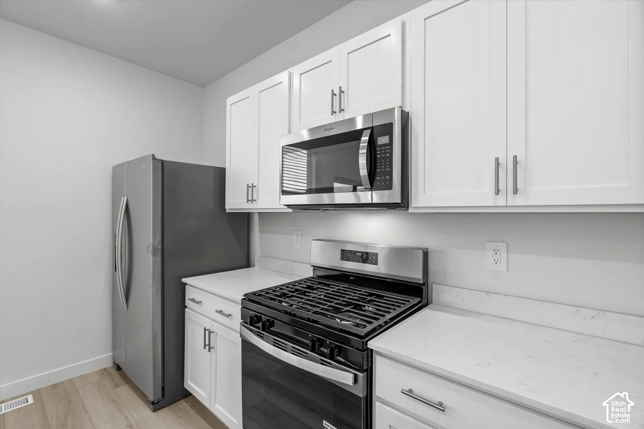 Kitchen featuring white shaker-style cabinetry, quartz countertops, stainless steel appliances, and wood-finish flooring